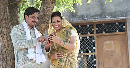 Rural Indian wife looking at her husband texting on mobile phone at village