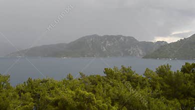 A storm with rain, thunderstorm and lightning looming on the Mediterranean Sea coast with mountains covered with forests near the