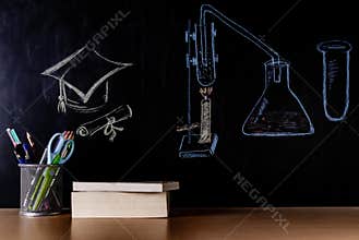 Unique front shot of a Square Academic Cap or Moratarboard with lab set-up drawn by chalk on blackboard and books placed on table