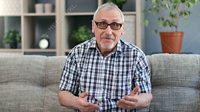 Portrait of smiling grandfather 80s blogger talking gesticulating online broadcasting on couch