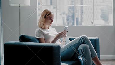Lady reads messages on mobile phone sitting on azure sofa