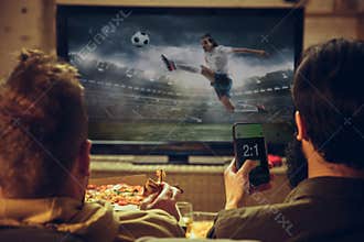 Men with betting application in phone. Group of friends watching TV, sport match together. Emotional fans cheering for