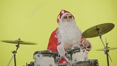 Santa Claus in festive costume with beard and sunglasses plays drums on yellow studio background. Man in a carnival
