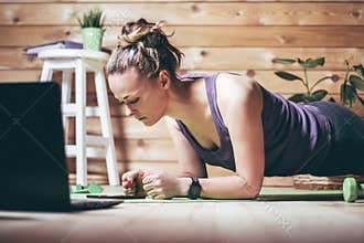 Woman in sportswear stands in plank near laptop. Home workout concept
