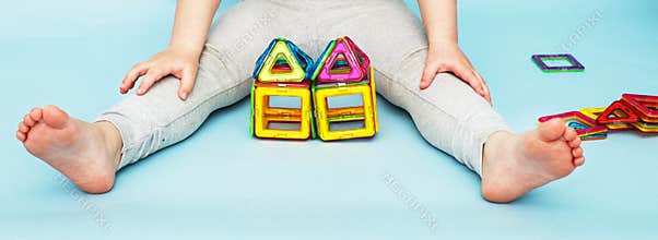 Little girl playing with colorful magnetic constructor toy on blue background. child built a house. banner
