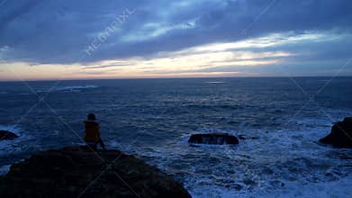 lonely woman in jacket sitting at the wavy sea with dramatic sky, loneliness
