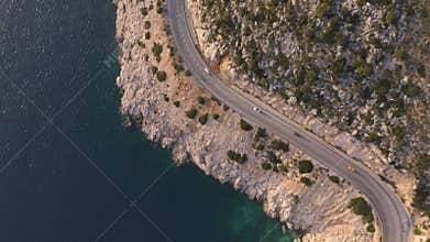 Birds eye view of asphalt mountain road with driving cars above the blue sea.