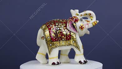 A white elephant figurine made of marble covered with a gold blanket with rhinestones spins on a dark background