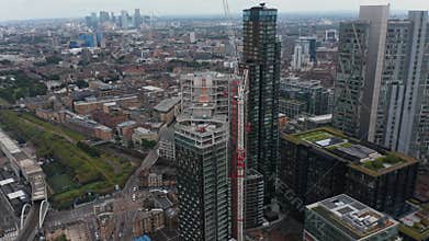 Fly around construction site of new skyscraper in Shoreditch district. Tilt up reveal cityscape. London, UK