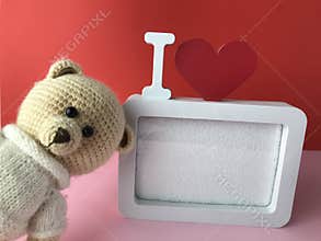 Soft knitted bear on a red background with a cute frame in white. romantic sentimental gift for a girl. a bear with black eyes
