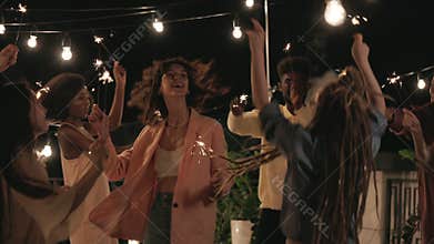 Multiracial friends having party on rooftop with sparkles