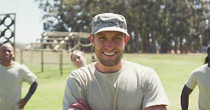 Portrait of caucasian male soldier in cap smiling at obstacle course with diverse group behind him