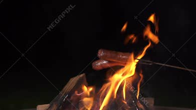 delicious sausages baked on a campfire in the forest. Frying small sausages over an open outdoor fire. hand frying
