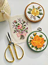 Vintage wooden embroidery hoops, scissors, needle, thread and fabric with floral cross-stitch embroidery on white