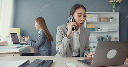 Young asia businesswomen talking on mobile phone and communicate sitting on office desk at workplace. Remote webinar, internet