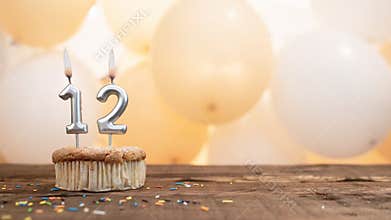 Happy birthday card with candle number 12 in a cupcake against the background of balloons. Copy space happy birthday for twelve