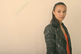 Studio shot of young Asian woman thinking while wearing leather jacket against white background