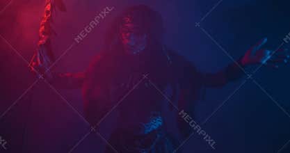 Creepy shaman with face paint is holding the staff and performing a ritual dance
