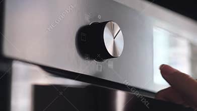 Close up of woman hand turning round temperature oven handle in the kitchen at home. Concept. Kitchen utensils for easy