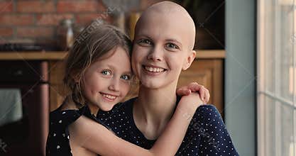 Bald sick mother cancer patient hugging with little daughter indoor