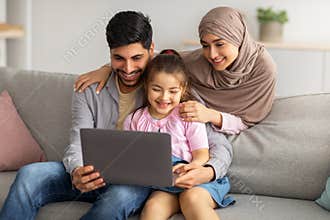Precious time with family. Happy muslim parents and cute little girl using laptop together, watching photos or movie