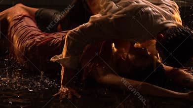 A sexy couple moves to the beat of the music in the pouring rain, and then lies on the surface of the water. Silhouettes