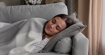 Serene woman sleeping on sofa under plaid in living room
