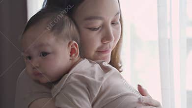 Asian woman mother parent embracing baby infant lull and calm baby down near window at home. mom holding newborn baby with love an