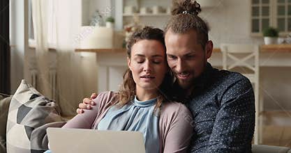 Happy affectionate bonding young married couple using computer.