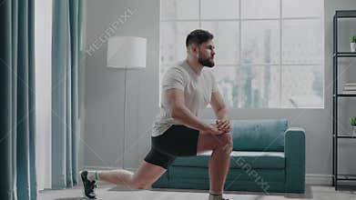 Muscular bodybuilder with beard stretches legs by sofa
