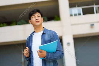 Portrait of a Asian college man student carrying a backpack and standing in a school hallway at campus