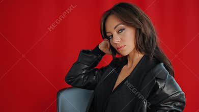 Chic brunette woman in black posing against red background