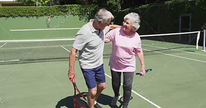 Happy caucasian senior couple embracing on outdoor tennis court in sun after playing a game