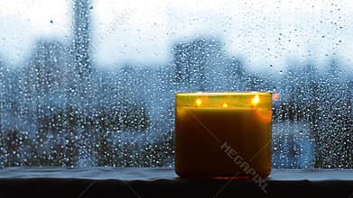 Burning aroma candle puts near by window that have rain drop