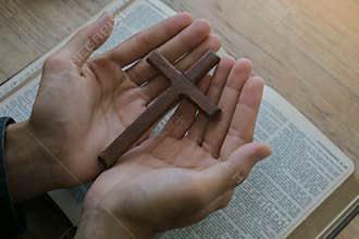 Christian man holding jesus cross.Hands folded in prayer on a Holy Bible on wooden table