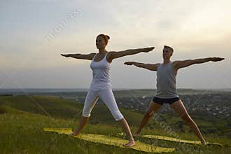 Middle aged man and woman doing Five Pointed Star practicing yoga on grassy hill in the morning