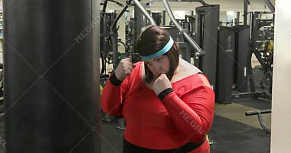 Fat woman trains with a punching bag in the gym.