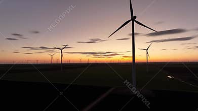 ?erial drone view of wind turbine at sunrise or sunset. The drone flies past the propellers