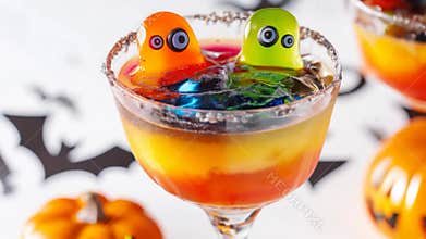 Colorful halloween cocktail is being served in a glass with a sugared rim and gummy candies. The drink is surrounded by
