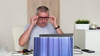 A man working on a laptop puts on glasses to see better