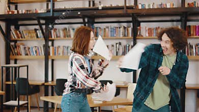 Girl and guy students study in class or library, they fight with papers and laugh. A guy and a girl are playing around