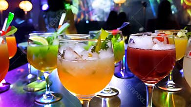 Several alcoholic cocktails on a bar counter and dancing people in the night club people.