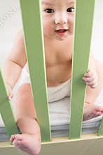 Baby in a diaper sitting in a crib