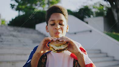 A cheerful boy is enjoying a burger outdoors wrapped in an American flag, reflecting patriotism and freedom while