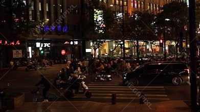 Vibrant Shanghai street and pedestrian crossing at night with people, scooters and cars. Illuminated buildings and