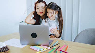 The mother and daughter enjoy a video call on their laptop. The daughter proudly shows her drawings to the camera