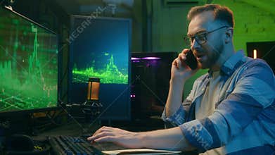 Positive Caucasian man worker male guy employer smile typing keyboard computer talking mobile phone. Happy crypto trader