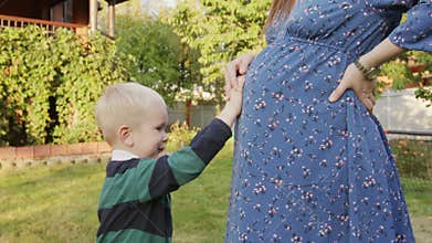 Little boy rubbing his pregnant mom's belly outdoor