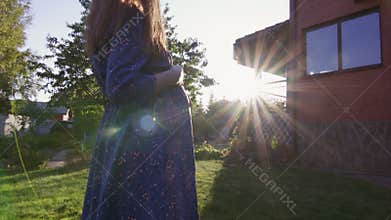 Beautiful pregnant woman enjoying fresh air at sunset rays on the backyard