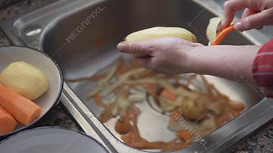 A woman washes potatoes under the tap of water in the kitchen and peels them